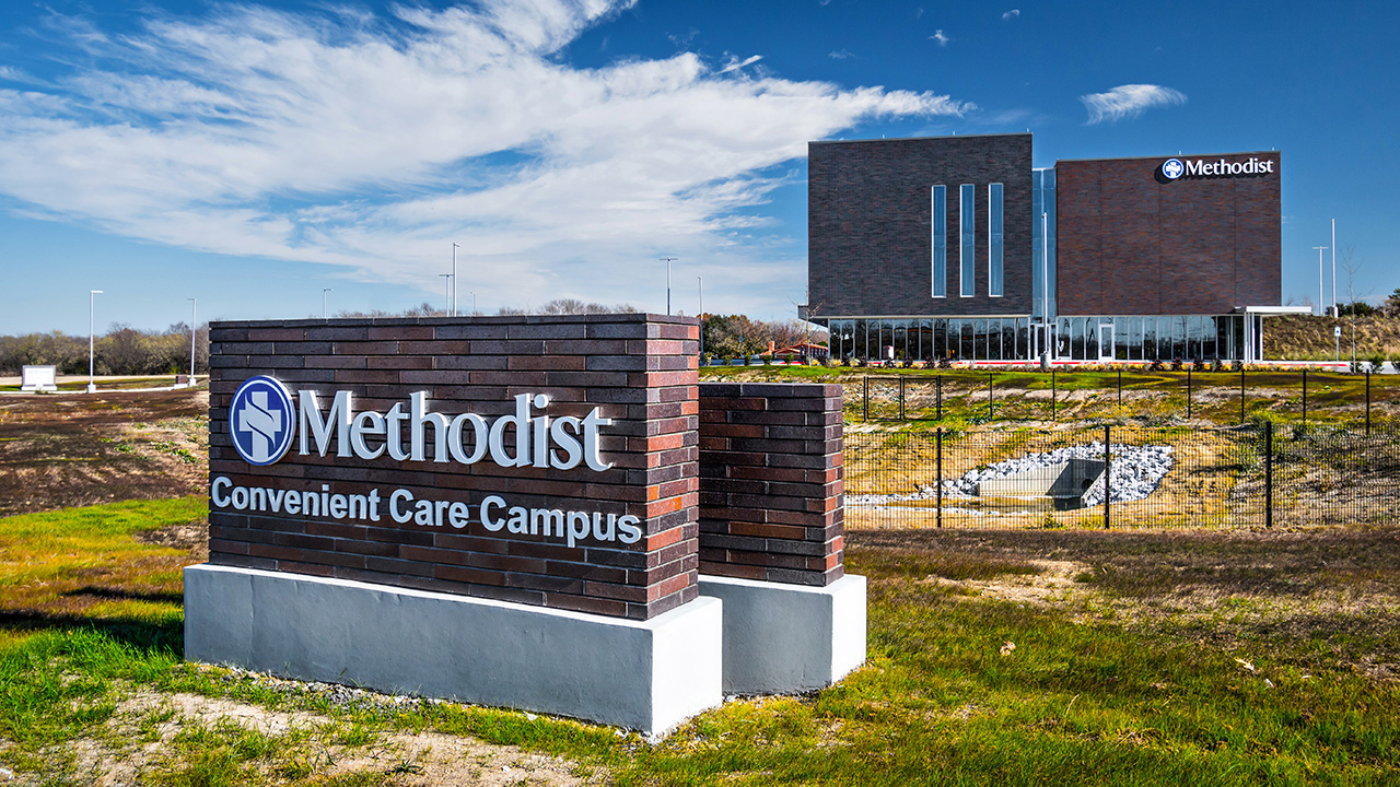 Image of a brick, multi-level healthcare facility. The facility is in the background, while the facility sign, is in the foreground.