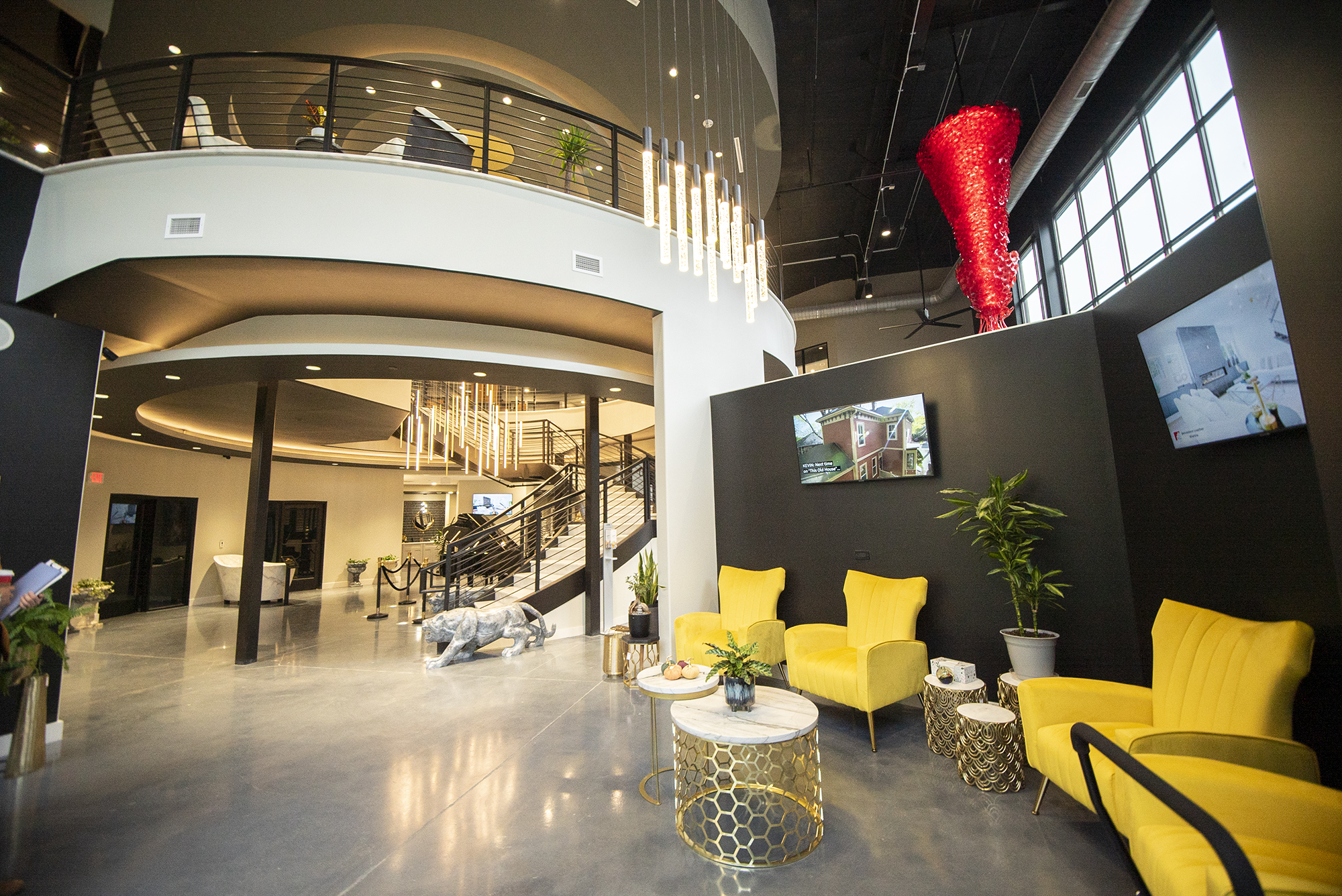 Stylish commercial interior featuring a modern two-story lobby with curved architecture, yellow lounge chairs, decorative lighting, polished concrete floors, and a dramatic red sculptural installation.