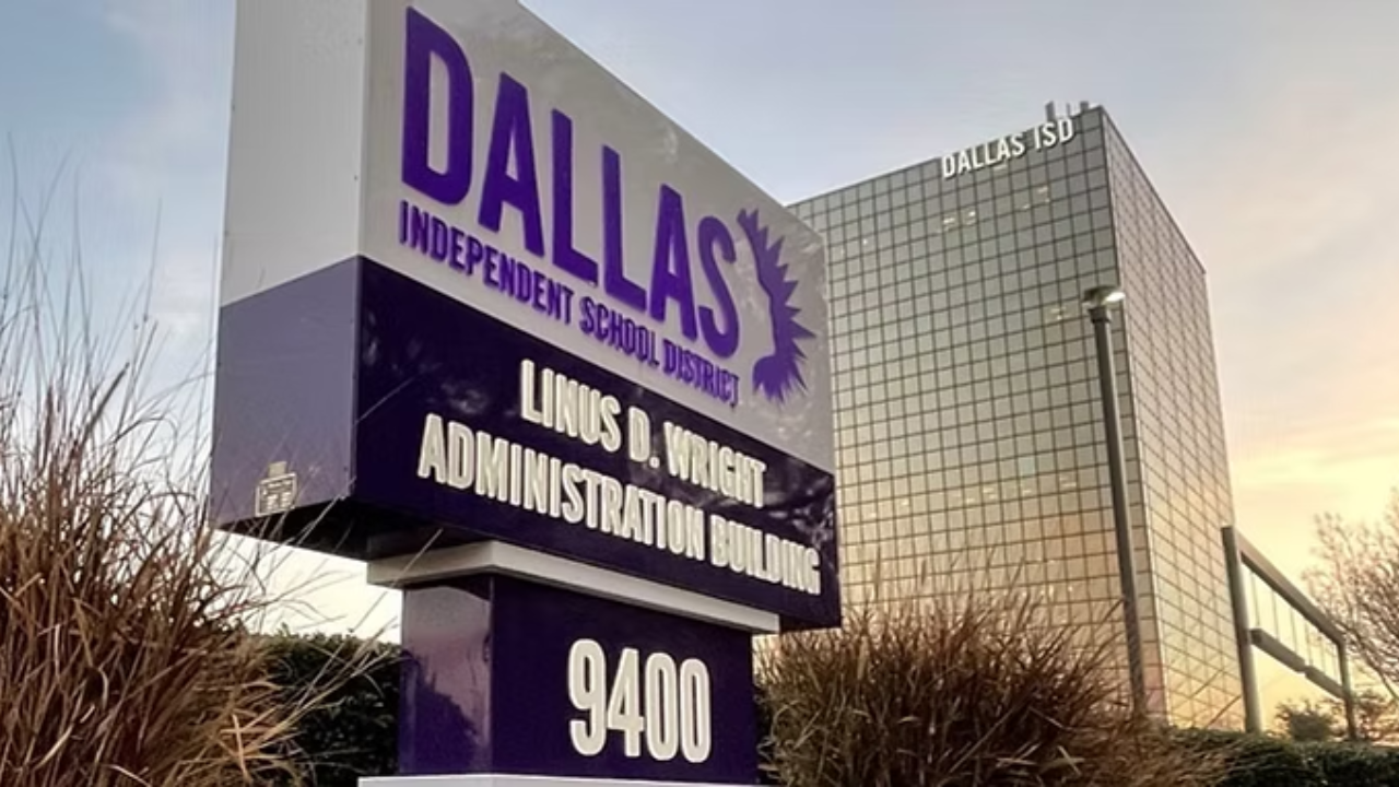Dallas Independent School District Linus D. Wright Administration Building sign in the foreground with the glass Dallas ISD headquarters building behind it at sunset.