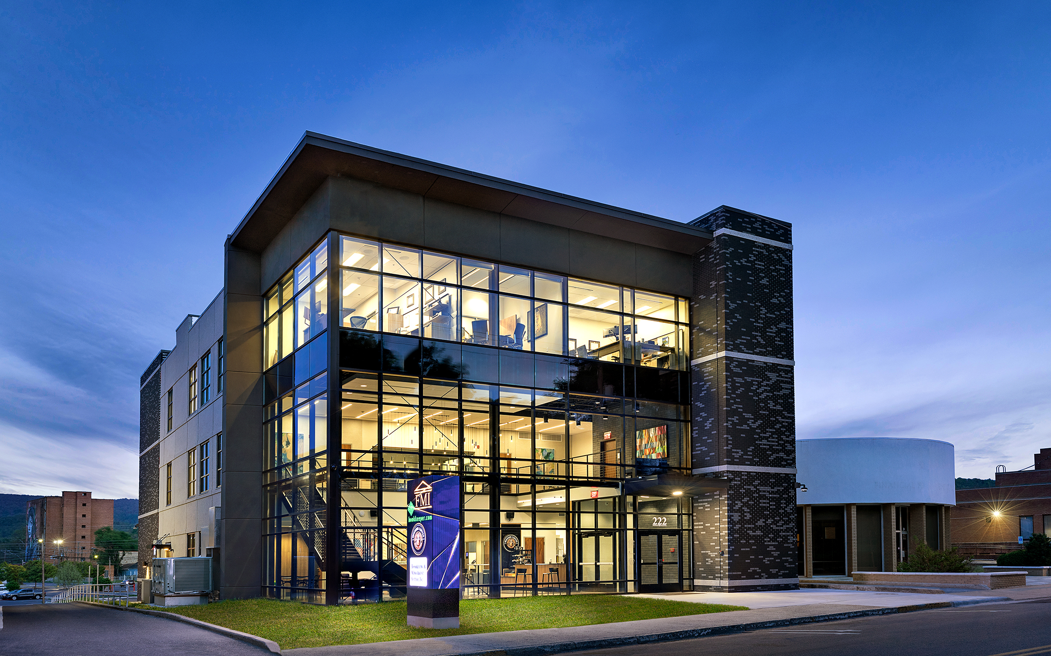 Evening view of a modern three-story glass and brick building with illuminated interior offices and signage for FMI, showcasing architectural lighting and transparency in design.