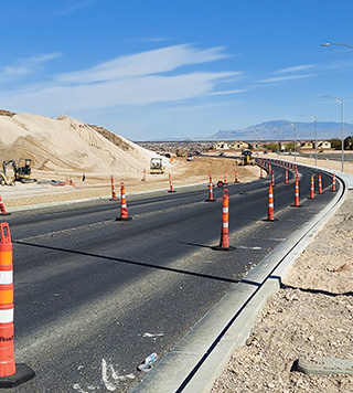 Roadway under construction. Roadway features many construction cones with large piles of dirt on both sides.