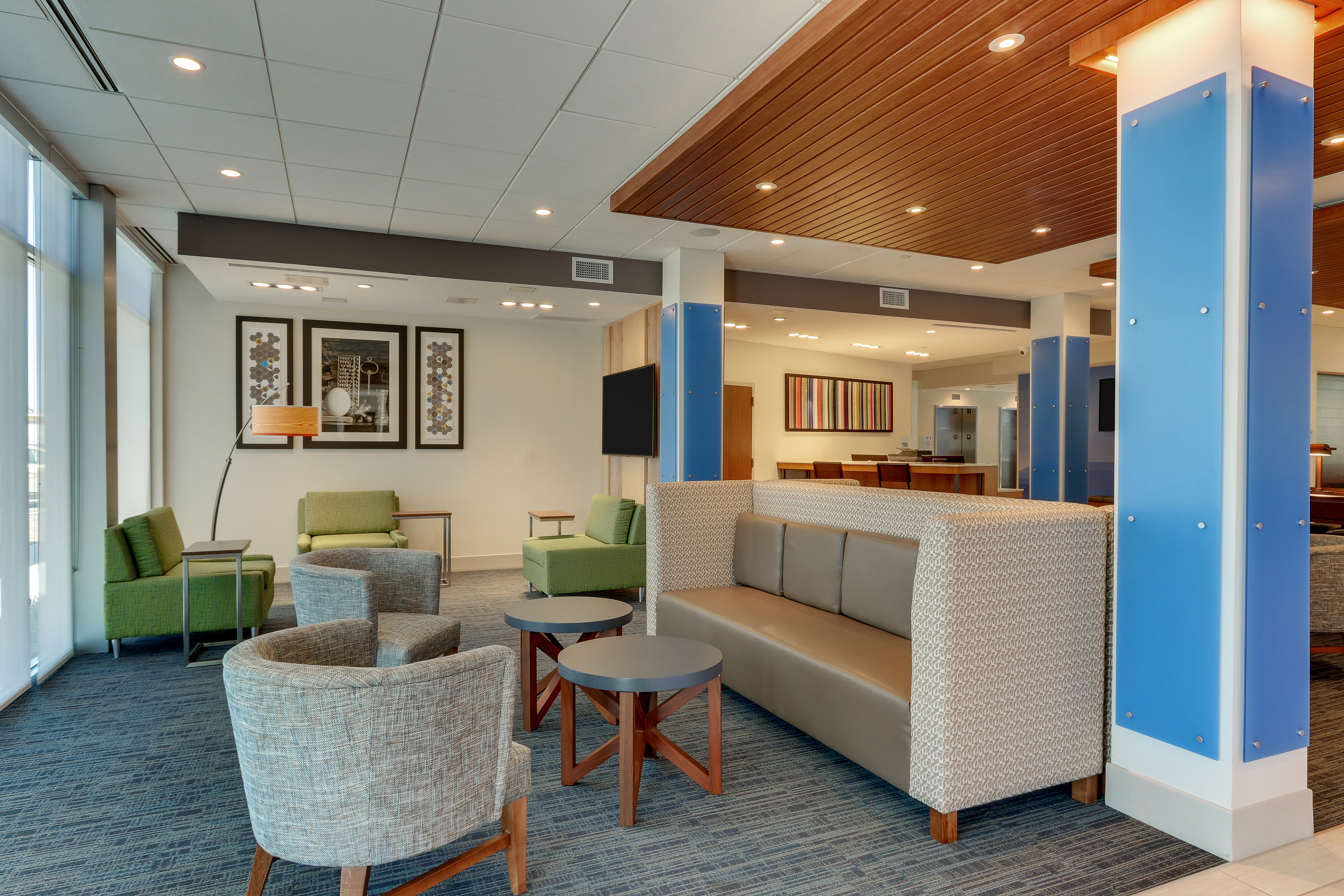 Modern hotel lobby with a mix of contemporary lounge seating, warm wood accents, blue columns, and vibrant wall art, creating a welcoming and stylish interior space.