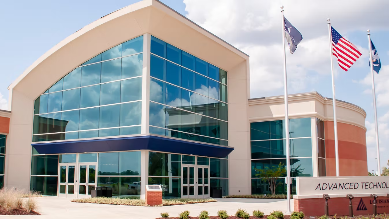 Exterior of the Advanced Technology Center featuring a modern glass facade, curved rooflines, and multiple flags displayed at the entrance under a partly cloudy sky.
