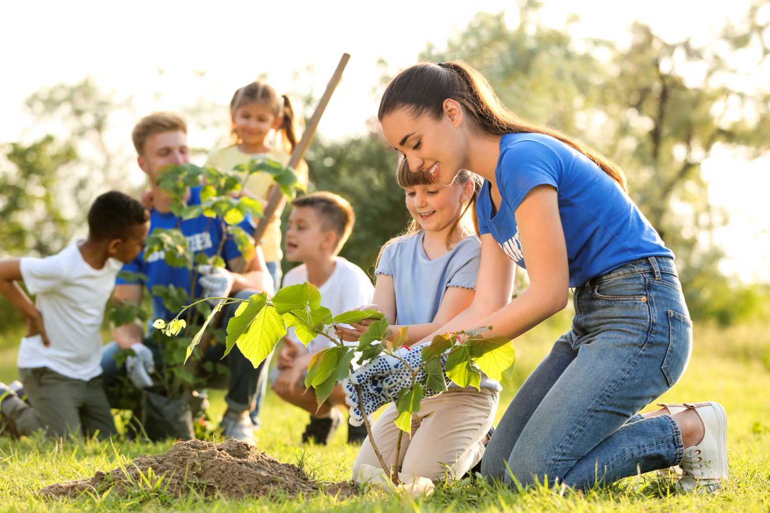 Women helping a young girl plant a tree in the ground